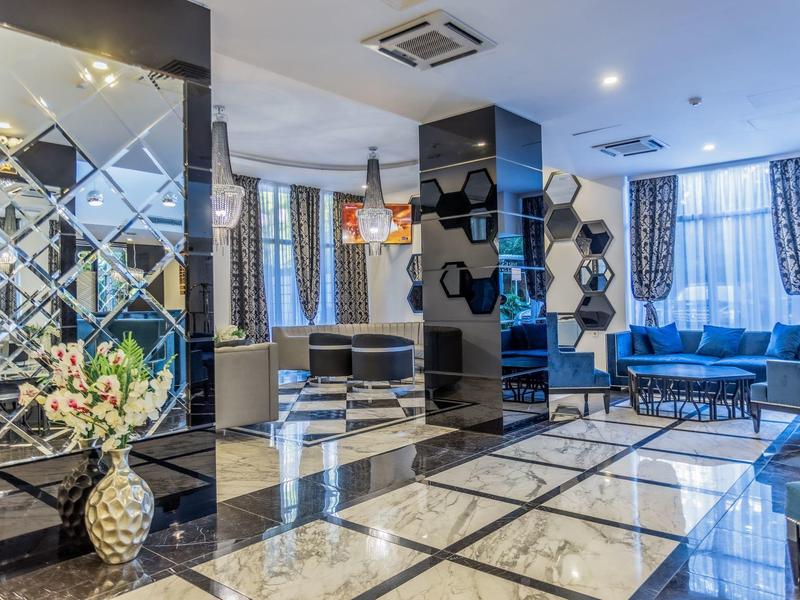 Luminoso vestíbulo de hotel con azulejos de mármol, paredes espejadas y mobiliario moderno con sofás y jarrones de flores.