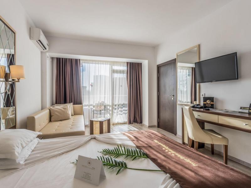 Habitación de hotel luminosa con cama, sofá, escritorio y balcón con vistas a la ciudad