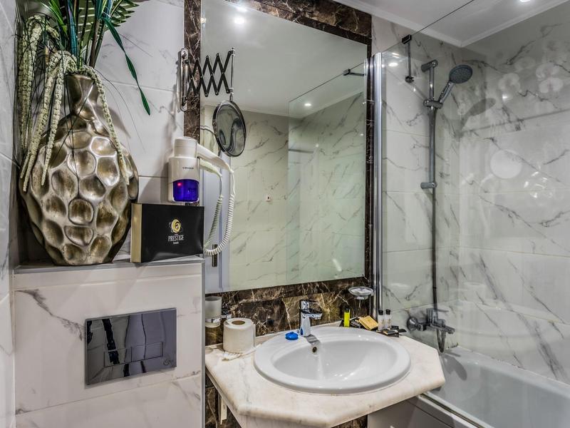 Baño moderno con paredes de mármol, lavabo y arreglo floral decorativo.