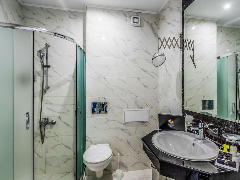 Baño moderno con ducha, inodoro y lavabo, mármol blanco y encimera negra.