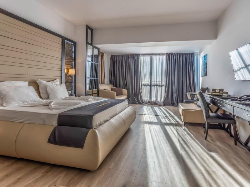 Habitación de hotel moderna con cama grande, escritorio y ventana panorámica con cortinas.