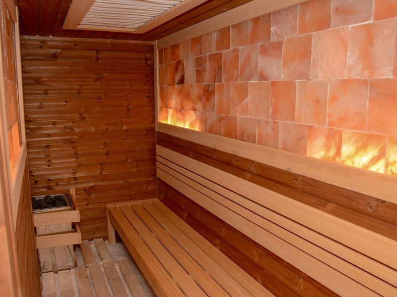 Sauna de madera con bancos largos y paredes de piedra de sal iluminadas