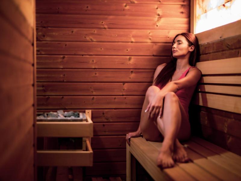 Mujer sentada relajada en una sauna de madera con luz tenue.