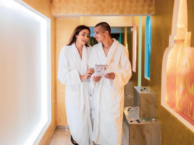 Pareja con albornoces relajándose y riendo en un pasillo de hotel.