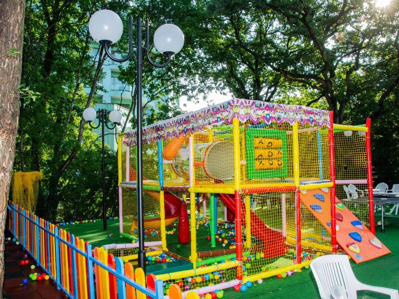 Colorida zona de juegos al aire libre con estructura para trepar y tobogán, rodeada de árboles.