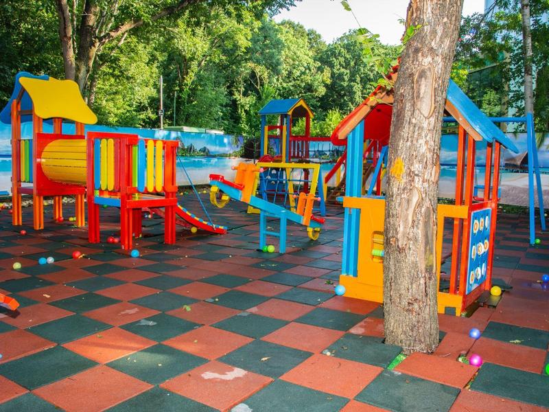 Colorida zona de juegos con diversos equipos en un área rodeada de árboles.