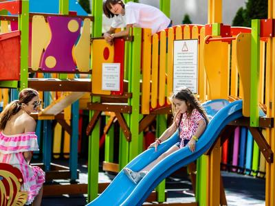 Kinderen spelen op een kleurrijke speeltuin met glijbaan en klimmende ouders.