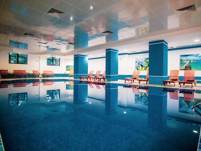 Overdekt zwembad met blauw water en ligstoelen langs de zijkanten in een hotel.