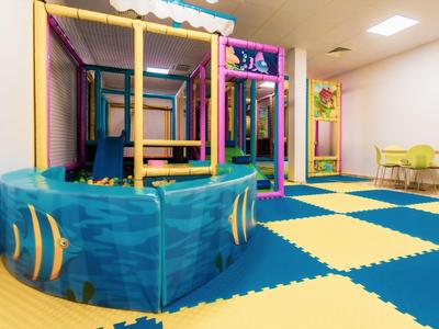 Goed verlichte speeltuin voor kinderen met klimrek en zachte kleurrijke vloerbedekking.