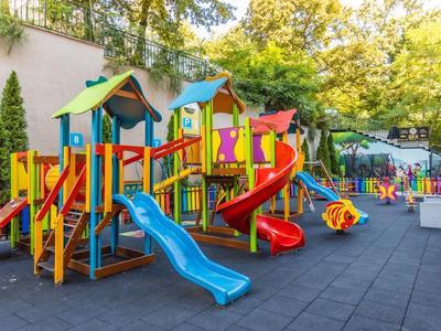 Kleurrijke buitenspeelplaats met glijbanen en klimrekken naast een muur.
