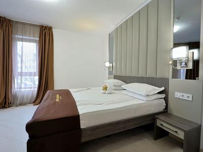 Moderne hotelkamer met tweepersoonsbed, nachtkastje en grote ramen met gordijnen.