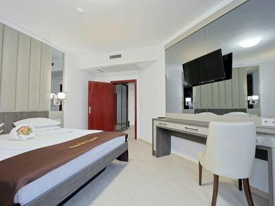 Modern hotelkamer met bed, bureau, stoel en aan de muur gemonteerde tv in lichte tinten.