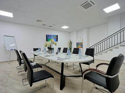 Moderne vergaderruimte met ovale tafel, zwarte stoelen en een scherm aan de muur.