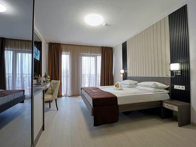 Moderne hotelkamer met tweepersoonsbed, stoelen en vloer-tot-plafond ramen met gordijnen.