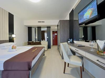 Modern hotelkamer met tweepersoonsbed, bureau, stoel en wand-tv.