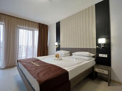 Moderne hotelkamer met tweepersoonsbed, grote ramen en beige gordijnen.