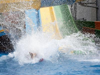 Glijbaan met grote waterspetter en persoon die het zwembad binnengaat.