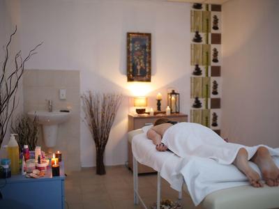 Persoon ontspant op massagetafel in rustige spa met kaarsen en handdoeken.