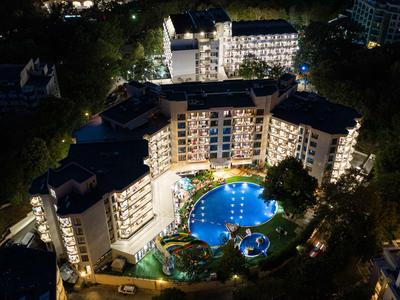 Nachtzicht op een hotel met verlicht U-vormig zwembad en omliggende gebouwen.