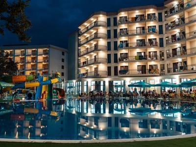 Hôtel illuminé avec piscine et aire de jeux aquatique la nuit.