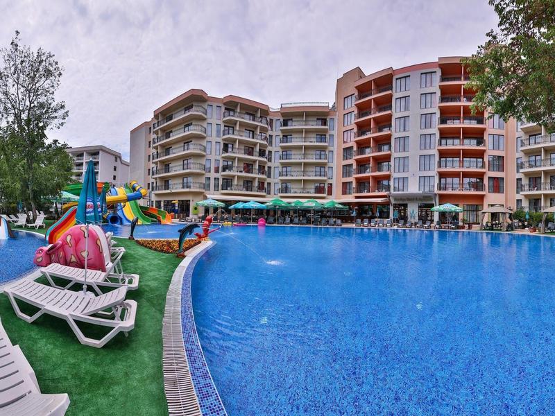 Groot buitenzwembad met ligstoelen en speelgedeelte voor een meerlaagshotel.