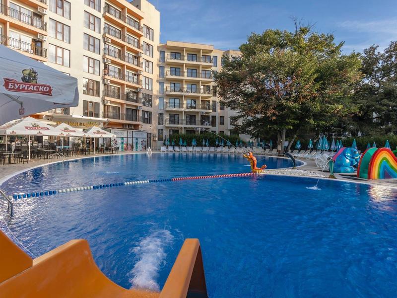 Groot hotelzwembad met glijbaan voor kinderen en parasols naast een meerlaagse gebouw.