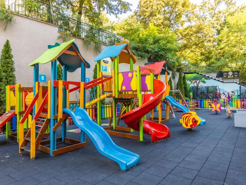 Kleurrijke buitenspeelplaats met glijbanen en klimrekken naast een muur.