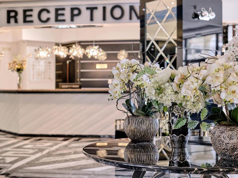 Hotelreceptie met elegante balie en decoratieve witte bloemstukken.