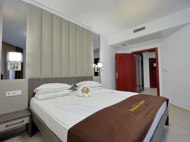 Moderne hotelkamer met tweepersoonsbed, grijze hoofdeinde en bruine deken.