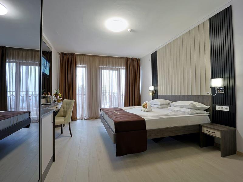 Moderne hotelkamer met tweepersoonsbed, stoelen en vloer-tot-plafond ramen met gordijnen.