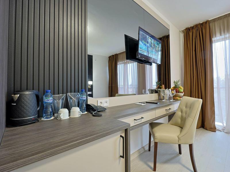 Modern hotelkamer met bureau, stoel, tv en raam met gordijnen.