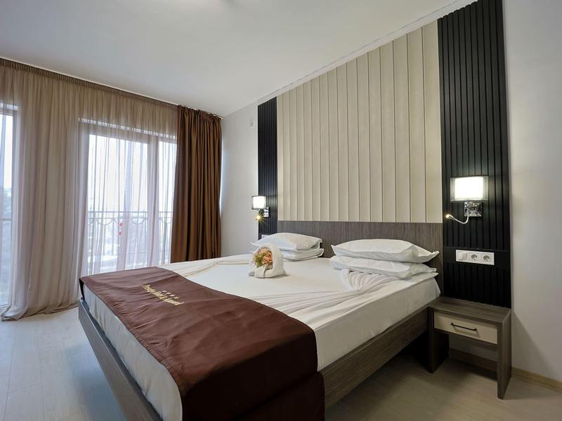 Moderne hotelkamer met tweepersoonsbed, grote ramen en beige gordijnen.