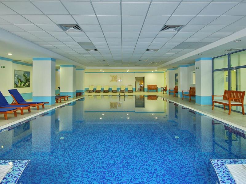 Groot, licht binnenzwembad met blauwe ligstoelen en glazen wanden.