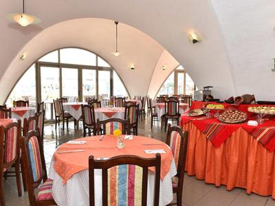 Restaurant met ronde tafels, oranje tafelkleed en houten stoelen in een gewelfde ruimte.