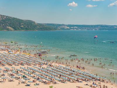 Wide sandy beach with sun loungers, mountains in the background, and people in the water