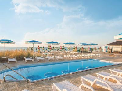 Hotel pool area with lounge chairs and umbrellas under a blue sky.