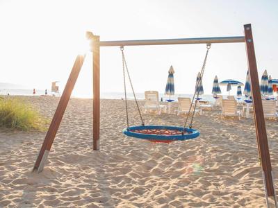 Sandiger Strand mit einer großen Nest-Schaukel aus Holz und blauen Sitzflächen.