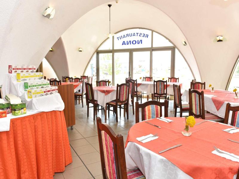 Licht restaurant met ronde tafels en oranje tafelkleden, buffettafel links.