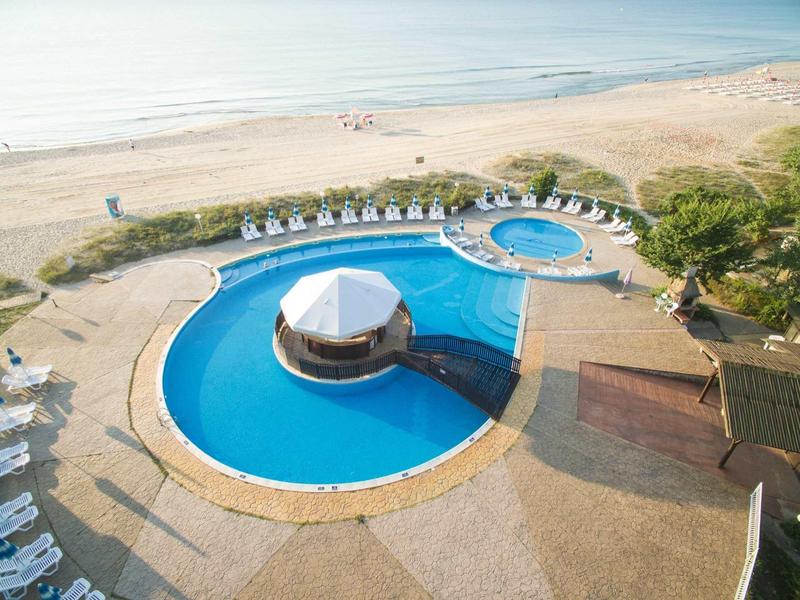 Groot zwembad met bar in het midden en toegang tot het strand op de achtergrond.