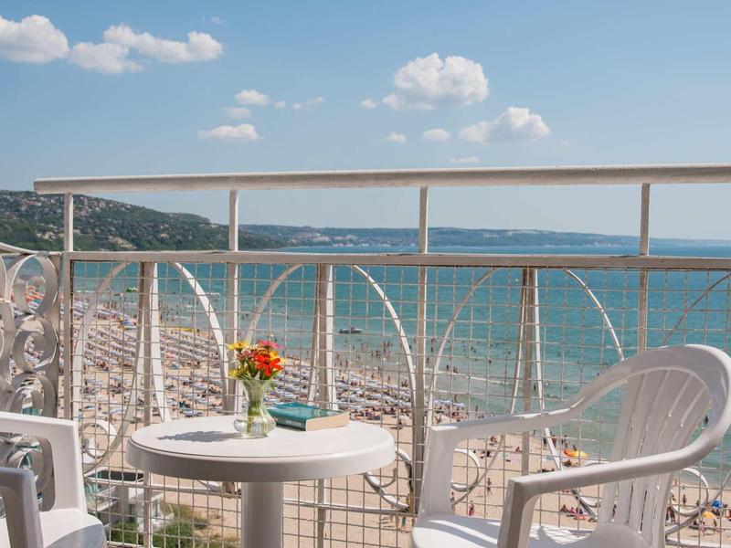 Balkon met witte stoelen en een tafel met bloemen, uitzicht op de zee en het strand.