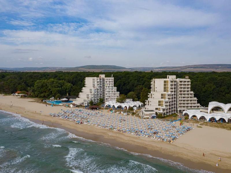 Hotelcomplex met hoge gebouwen op zandstrand naast bosrijk gebied onder bewolkte lucht.