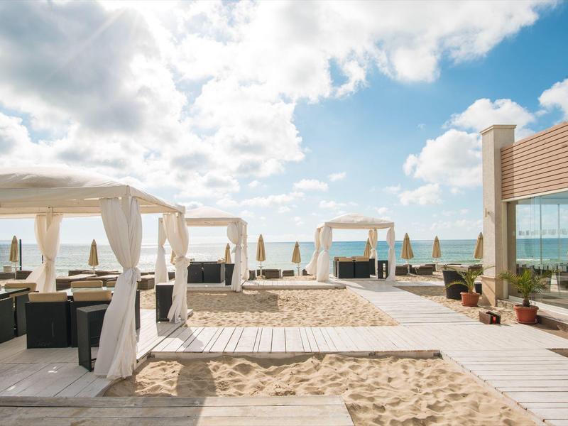 Offener Strandbereich mit weißen Pavillons und Blick auf das Meer bei sonnigem Himmel.