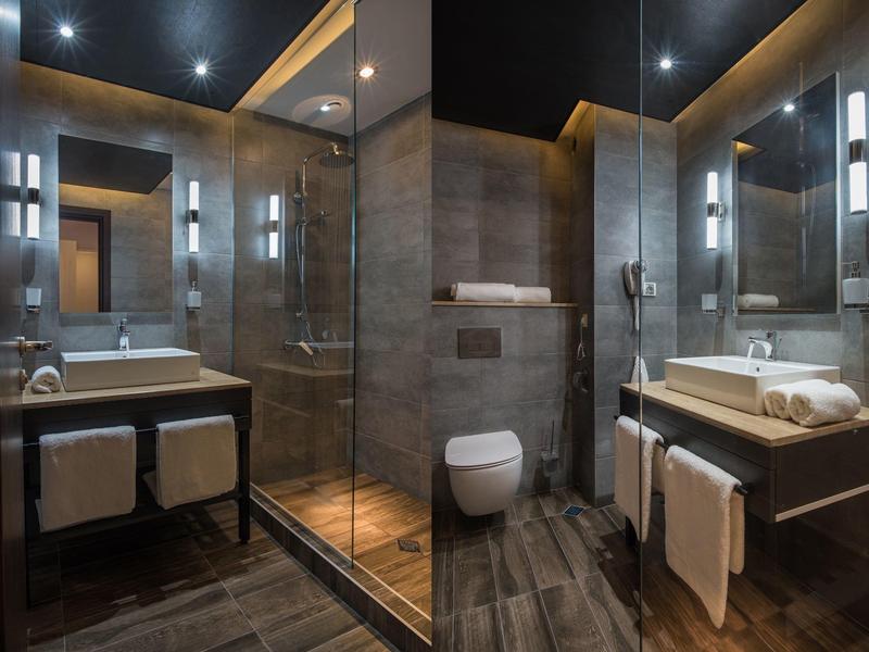 Modernes Badezimmer mit Glasdusche, Toilette, Waschbecken und dunklem Holzboden in einem Hotel.