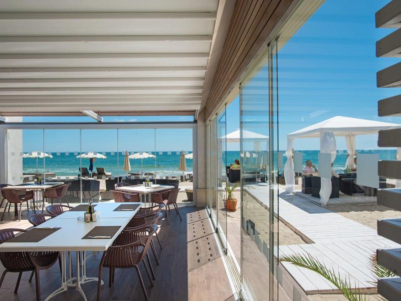 Modernes Restaurant mit Außenterrasse und Meerblick unter blauem Himmel.