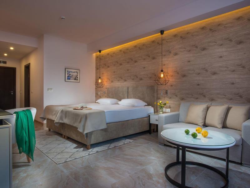 Modernes Hotelzimmer mit Doppelbett, gemütlicher Sitzecke und warmem Holzdekor an der Wand.