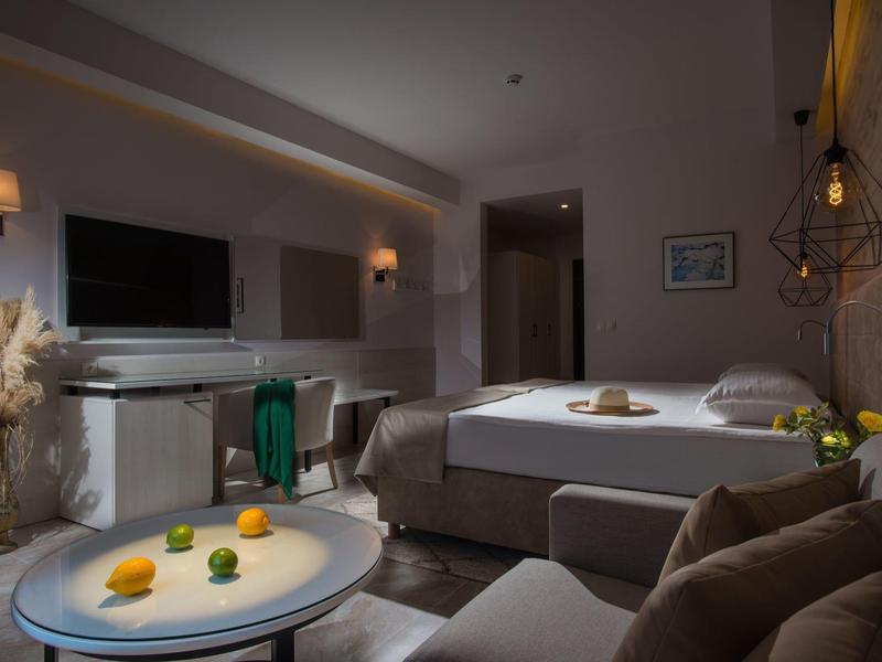 Modernes Hotelzimmer mit Doppelbett, Couch, Tisch mit Obst und TV an der Wand.