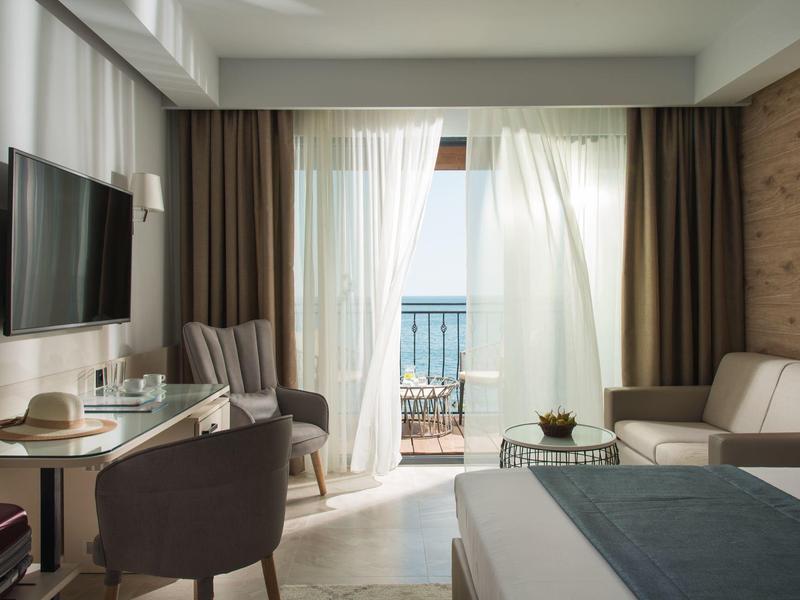 Modernes Hotelzimmer mit Balkon, Blick aufs Meer, Sitzbereich und Fernseher.