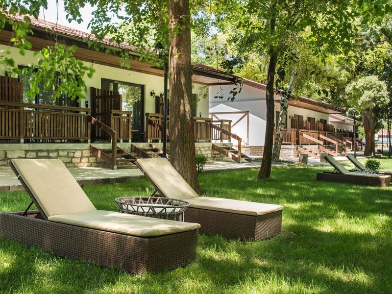 Zwei Liegestühle auf einem grasbewachsenen Hof neben einem Gebäude mit Bäumen im Hintergrund.