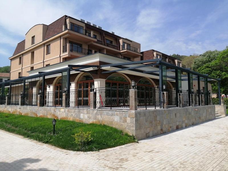 Modernes Hotelgebäude mit großem Glasvorbau und steinernem Fundament, umgeben von Grün.