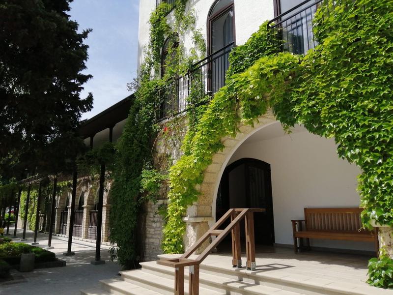 Ein Gebäude mit weißen Wänden und grünen Pflanzen, die den Eingang mit Bogen überwachsen.